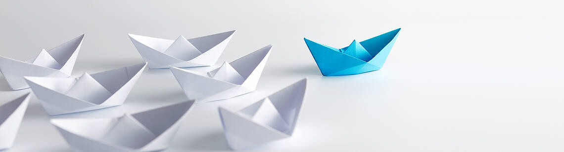 Viele weiße und ein blaues Papierschiff