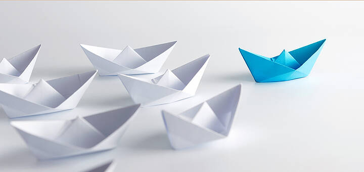 Viele weiße und ein blaues Papierschiff