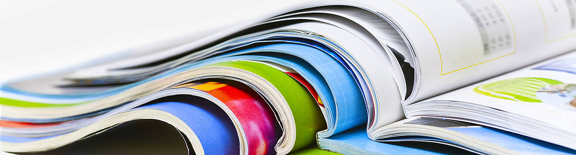 Mehrere Broschüren liegen aufgeschlagen aufeinander